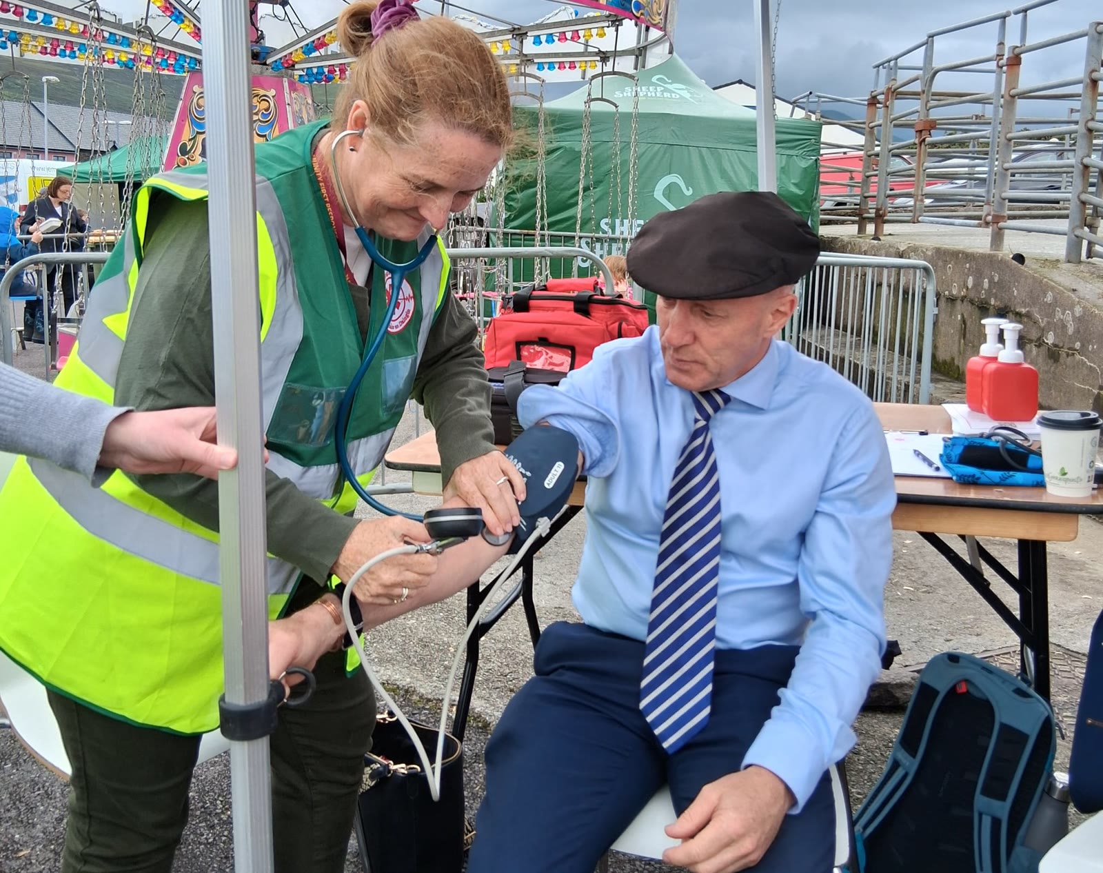 A woman in a high-visibility vest checks a man's blood pressure at an outdoor community event