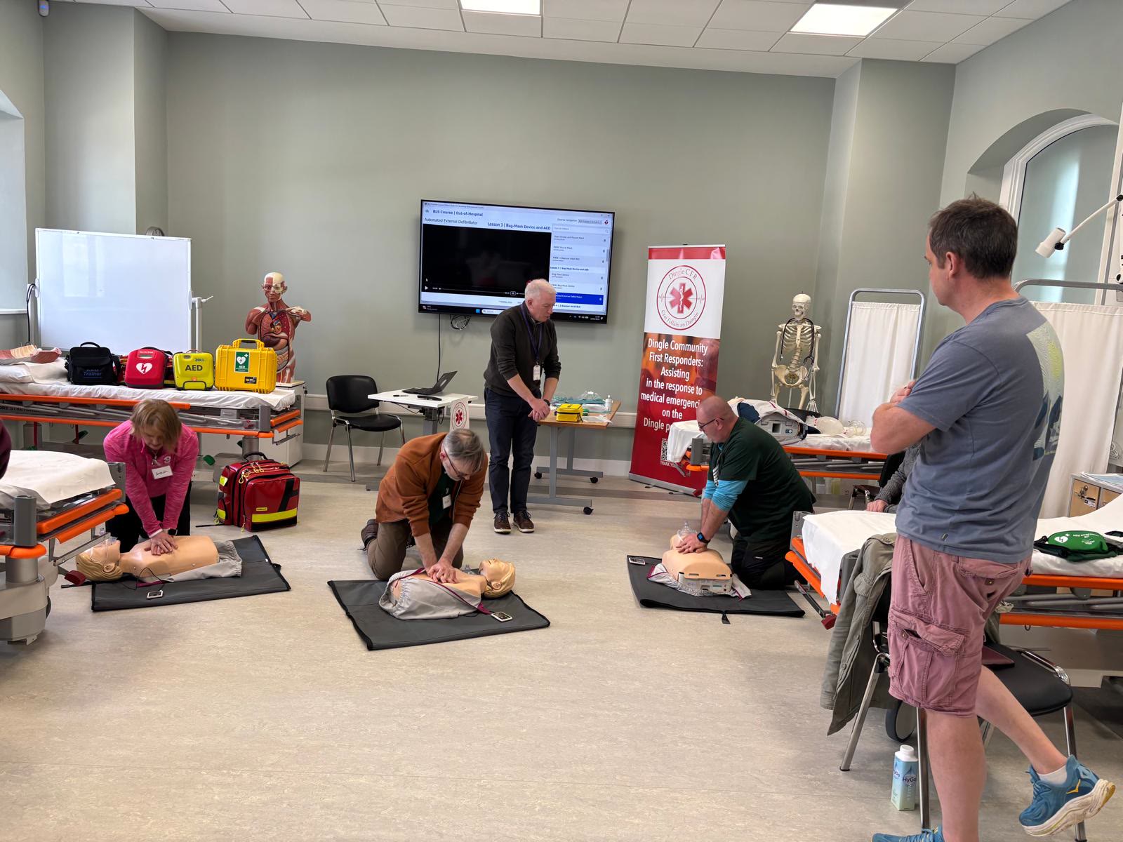 Three trainees practising chest compressions on manikins while an instructor watches
