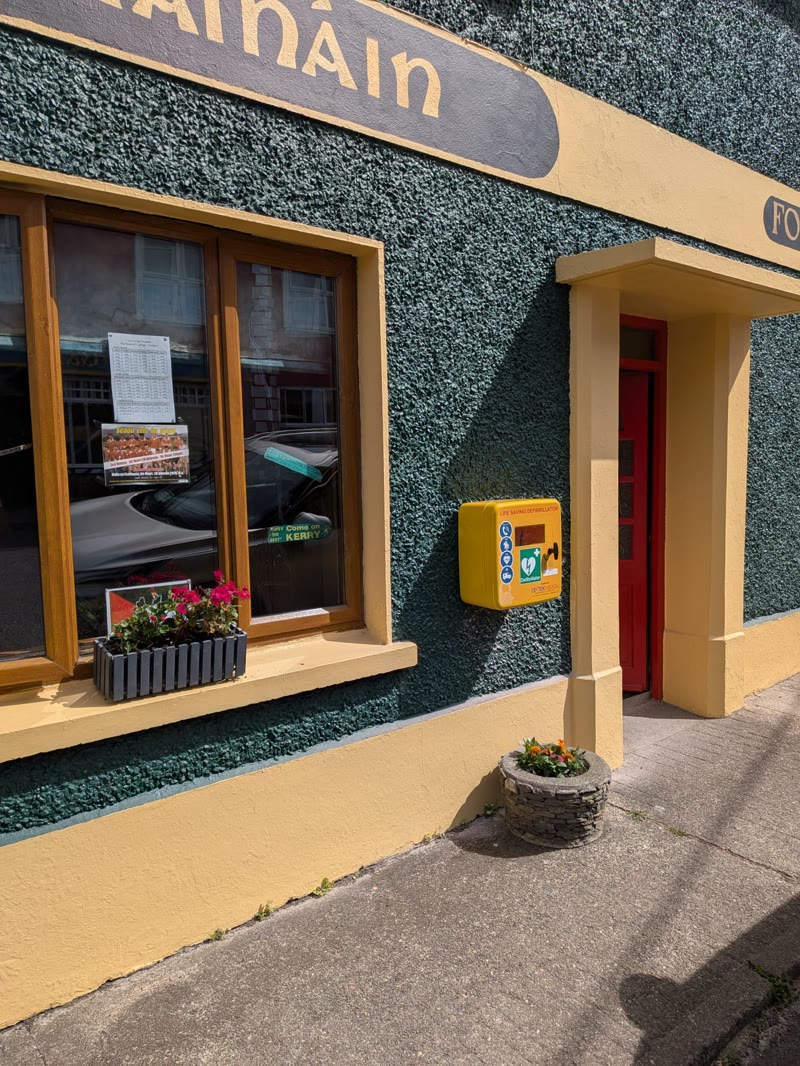 A yellow public access AED cabinet mounted on a shop front in Dingle