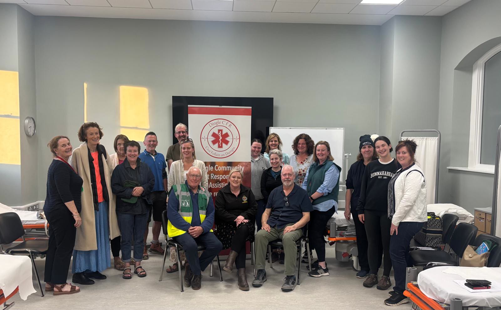 Dingle Heart Safe volunteers, some standing and some seated, gathered in front of a Dingle CFR roll-up banner