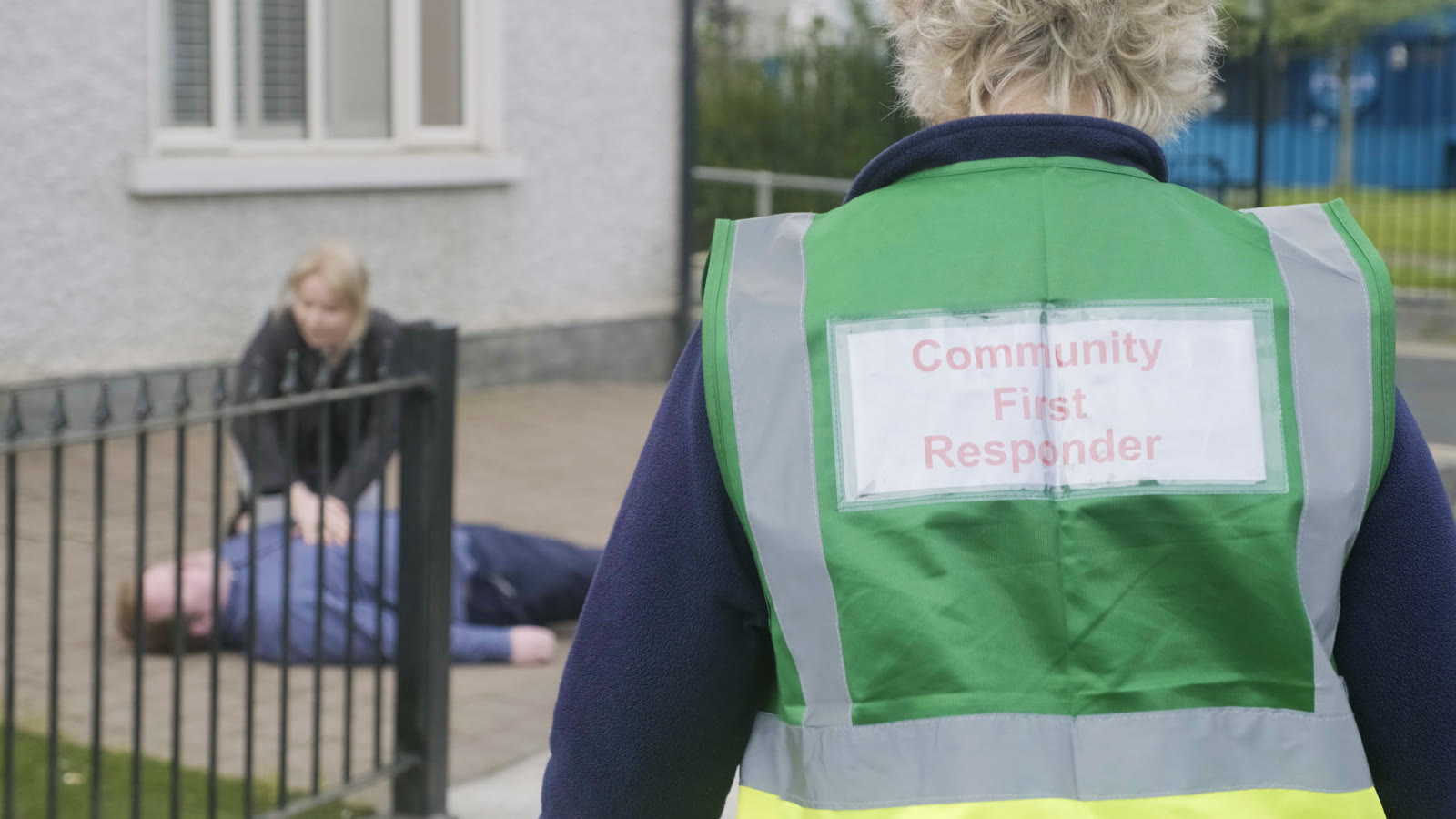 Close-up of a Community First Responder's vest, with CPR under way in the background