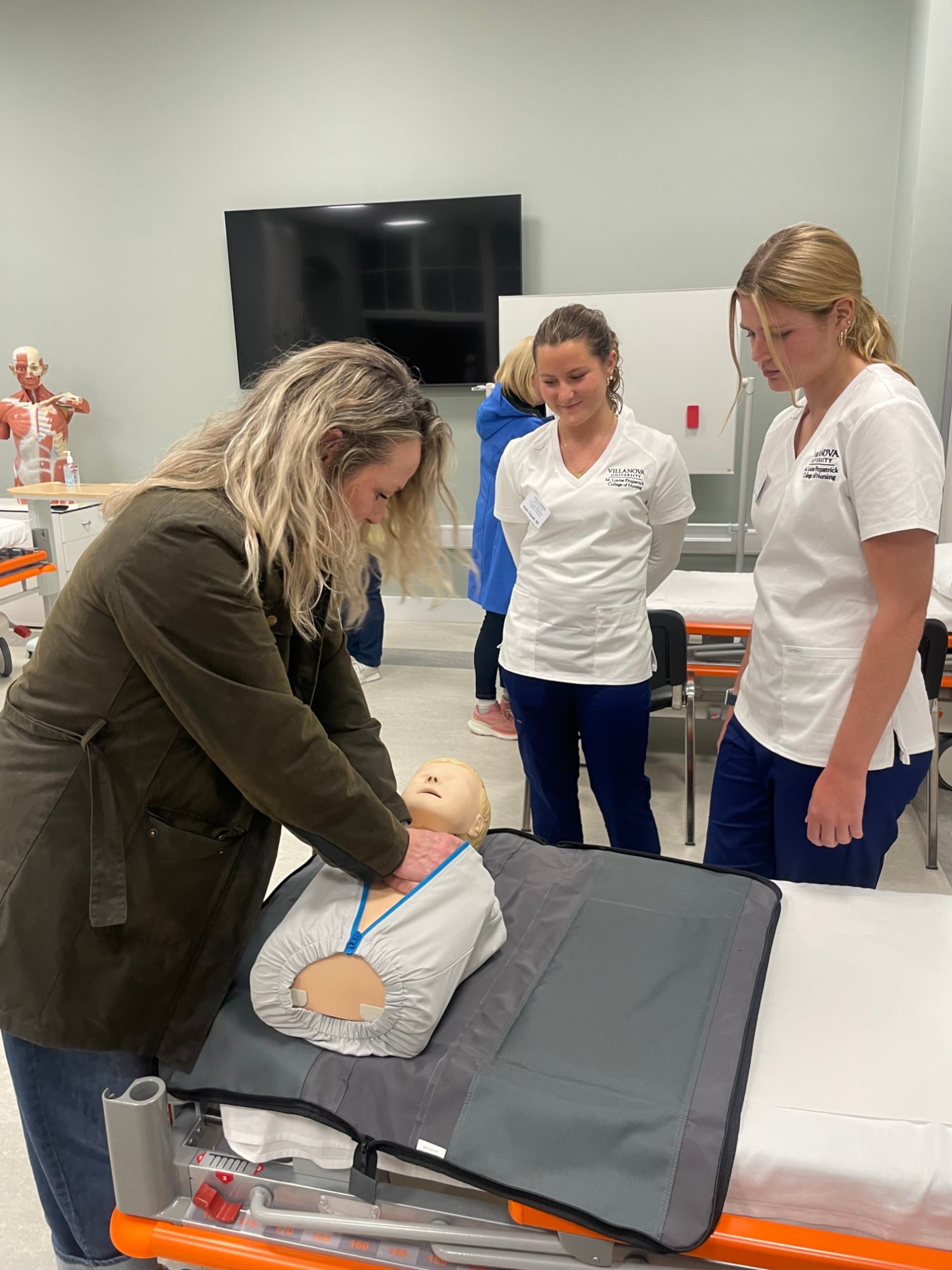 A workshop participant practises chest compressions on a manikin while two nursing students watch